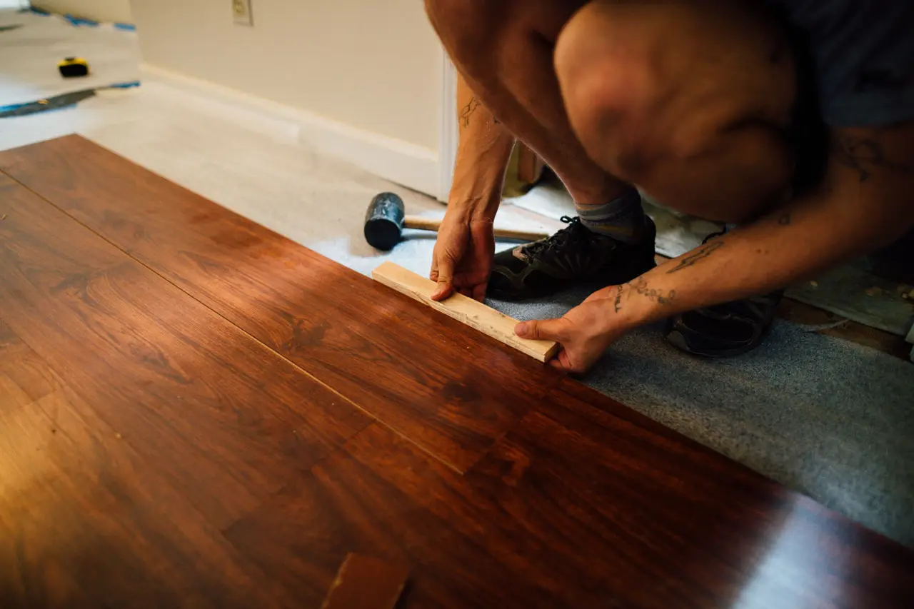 A flooring installer fitting a plank of luxury vinyl flooring into place in a bright living room