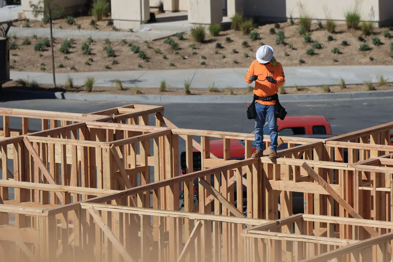 A general contractor in a hard hat reviewing plans on a clipboard at a framed-out job site