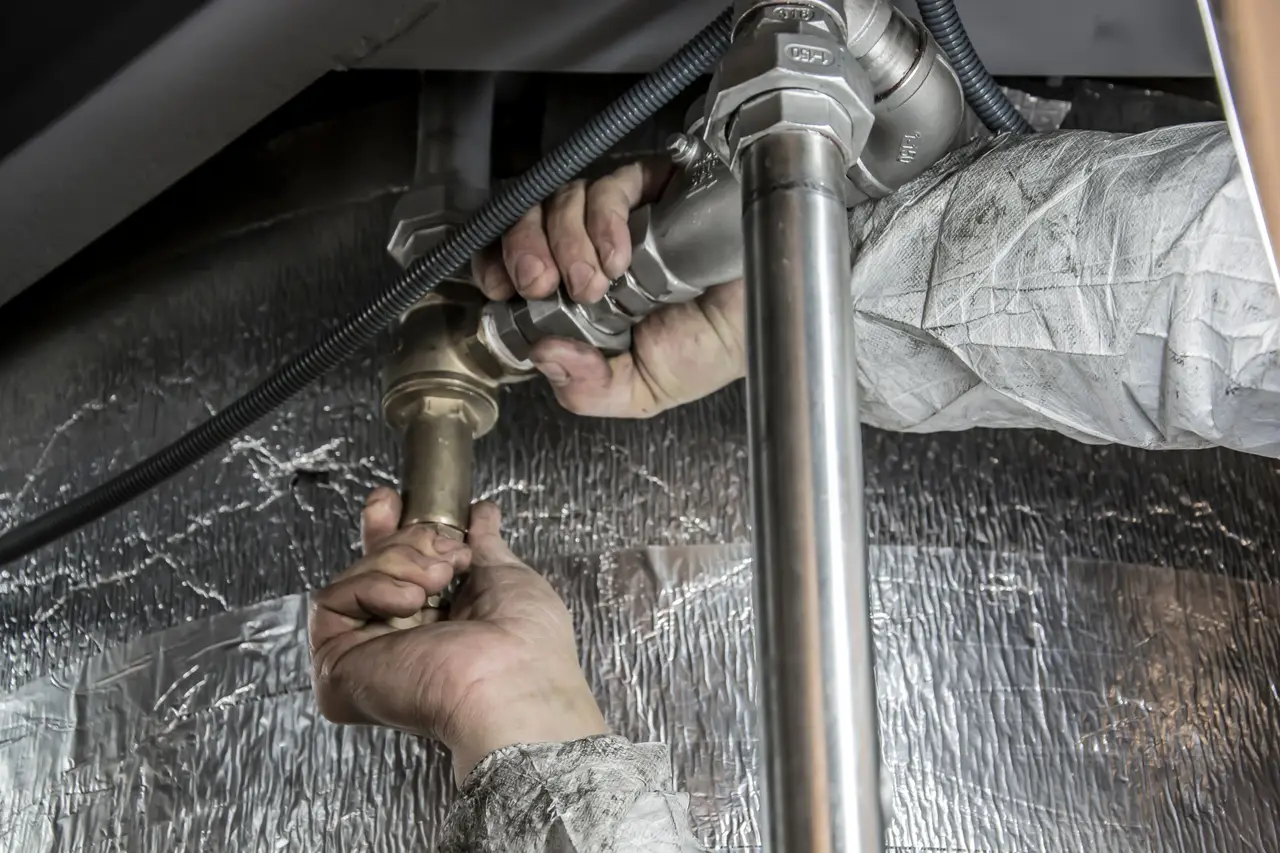 A plumber kneeling under a sink tightening a fitting with a wrench