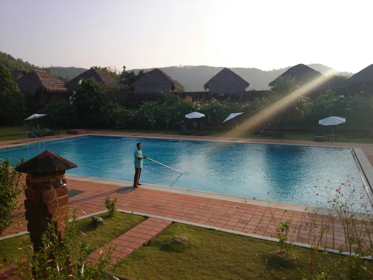 A pool technician skimming and testing the water of a backyard swimming pool on a sunny day