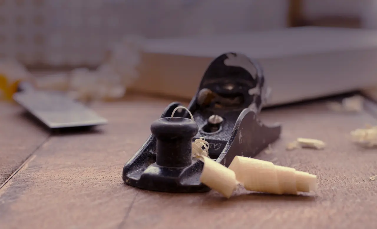 A craftsman's hands guiding a hand plane across wood, shavings curling up from the blade